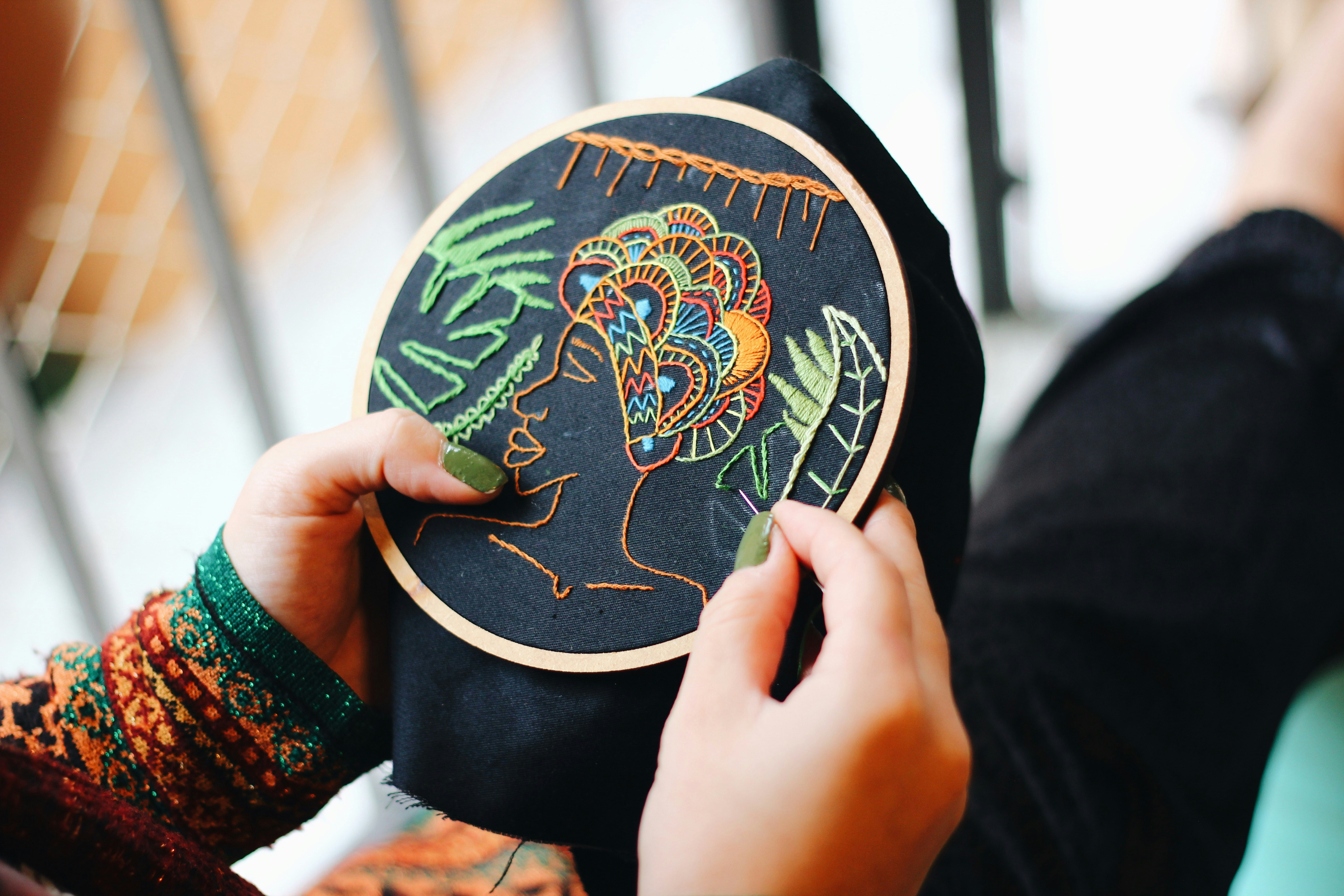Hands holding an embroidery hoop with colorful stitched patterns