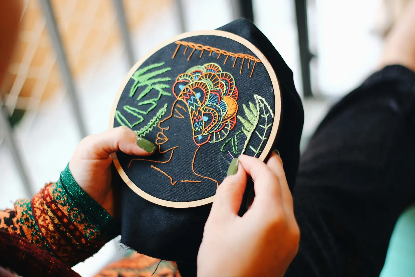 Hands holding an embroidery hoop with colorful stitched patterns